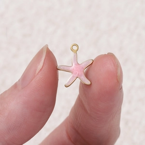 Pendentif étoile de mer en émail rose et acier inoxydable doré montré sur les doigts