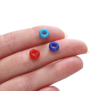 Vue macro de perles en acrylique colorées de 4x7 mm à grands trous sur un doigt