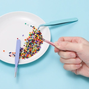Gros plan de pincettes de précision pastel ramassant des perles colorées pour bijoux DIY