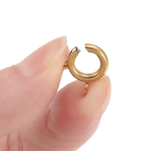 Close-up of a small gold spring ring clasp for jewelry making held between fingertips