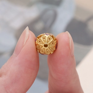 Détail macro d'une perle ajourée en cloisonné avec émail violet entre les doigts