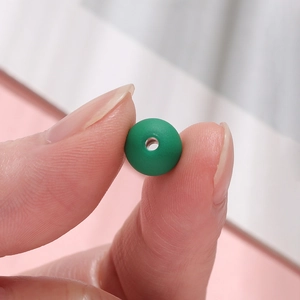 Macro detail of a 10mm matte green acrylic bead held between fingers for DIY crafts