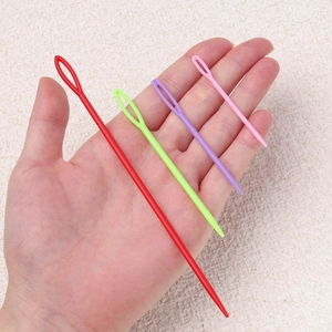 Detail of four colorful plastic large-eye sewing needles in varying sizes on a hand