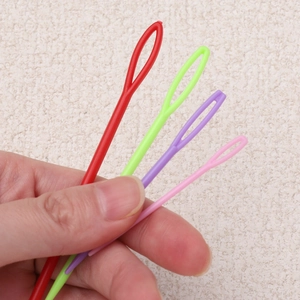 Detail of colorful plastic darning needles with large eyes held by hand for scale