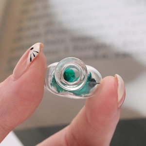 Macro detail of a mini glass wishing bottle with green dried flowers for DIY pendants
