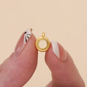 Close-up of small matte gold hollow round charm held between fingers for size reference