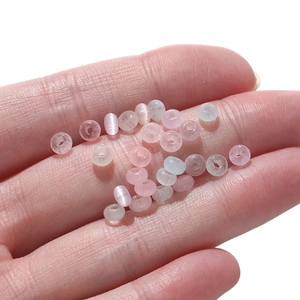 Close-up of 2x4mm pink and blue glass cat eye beads held in hand for DIY jewelry making