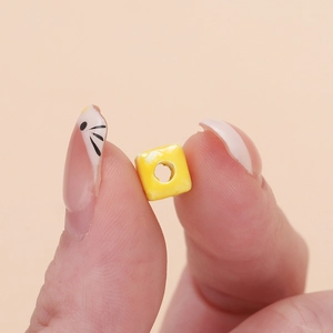 Close-up of a 6.5mm yellow square ceramic bead with a center hole for DIY jewelry making