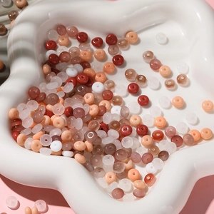 Vue macro de perles en verre 3x6mm aux couleurs chaudes sur un plateau en céramique blanc