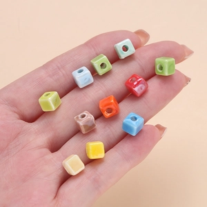 Macro view of colorful 6.5mm square ceramic beads with holes held in a person's hand