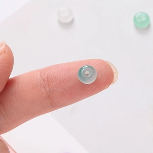 Vue macro d'une perle de verre vert pâle 3x6mm sur le bout d'un doigt pour bijoux DIY