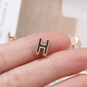 Macro shot of 10mm gold alloy letter H bead with black enamel finish on fingertips