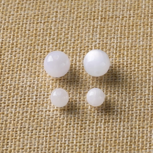 Macro shot of white pearlescent resin beads in two sizes on a woven mat for DIY jewelry
