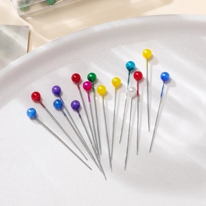 Close-up of multicolored pearl head sewing pins scattered in a white textured tray