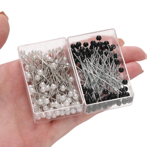 Detailed view of black and white pearl head pins in clear storage boxes for sewing