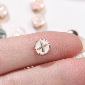 Detalle de una cuenta redonda de esmalte blanco con letra X dorada sobre el dedo