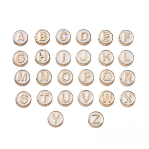 Vista macro de 26 cuentas redondas de esmalte con letras y borde dorado para joyería DIY