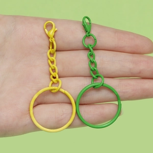 Hand hält gelbe und grüne Schlüsselanhänger aus lackiertem Metall mit Karabinerverschluss