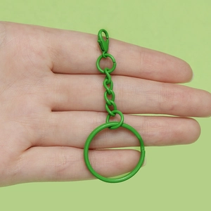 Detail eines mattgrünen Karabiner-Schlüsselanhängers mit Kette in der Hand gehalten