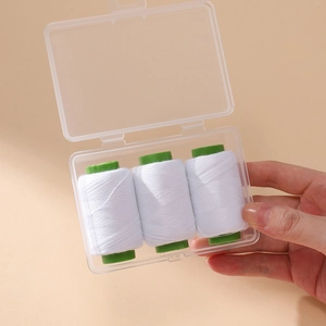 Portable sewing thread set with three white spools in a clear storage box held in hand