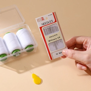 Detail showing 16 gold-eye needles with a needle threader and white sewing thread