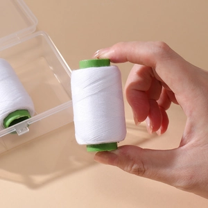 Close-up of white sewing thread on green spool with transparent storage box