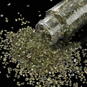 Close-up of olive green iridescent glass shards poured from a clear bottle for DIY crafts