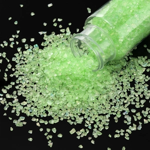 Macro view of light green iridescent glass gravel pouring from a clear bottle