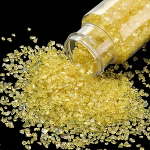 Macro shot of iridescent yellow crushed glass gravel pouring from a transparent jar