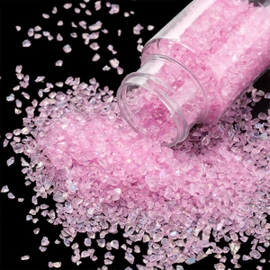Close-up of iridescent pink-purple glass gravel pouring from a clear bottle for DIY crafts