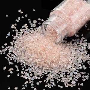 Close-up of iridescent pink glass gravel pouring from a bottle onto a black mirror