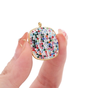 Close-up of a square gold pendant featuring colorful rhinestones held in hand