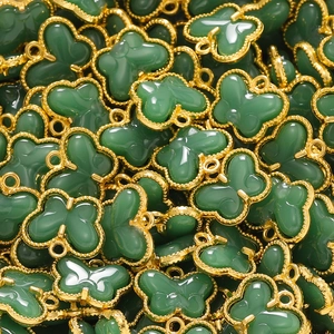 Macro view of butterfly charms with emerald resin and gold-plated beaded metal frames