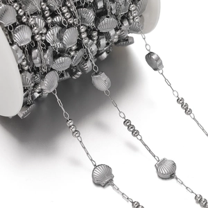 Macro detail of stainless steel chain with shell charms on a white spool for DIY jewelry