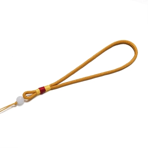 Détail du cordon tressé jaune avec accents de soie rouge et une perle de jade blanc