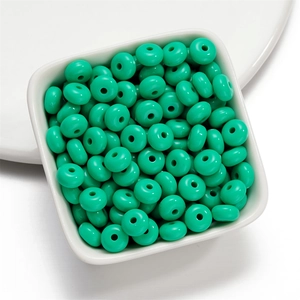 Macro detail of 8mm light green acrylic donut beads in a white square tray for DIY jewelry