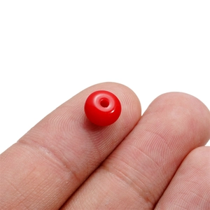 Macro shot of 8mm red acrylic spacer bead on fingertip for scale on white background
