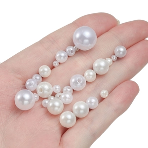 Close-up of assorted sizes of white ABS faux pearls with pre-drilled holes in a person's palm