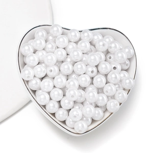 Close-up of white round ABS imitation pearls with holes in a heart-shaped ceramic dish