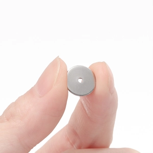 Detailaufnahme einer kleinen flachen Abstandsperle aus Edelstahl, die von Fingern gehalten wird