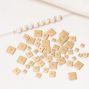 Macro shot of gold square spacer beads with center holes on textured fabric with pearls