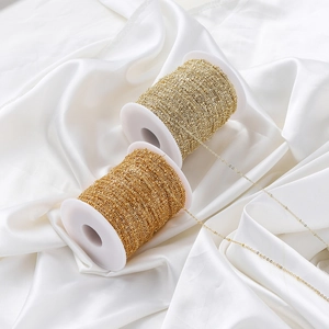 Detailed macro of two gold beaded chain spools for DIY jewelry making on white silk