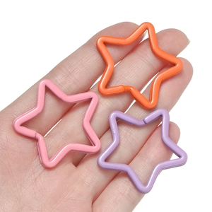 Hand holding colorful star-shaped metal keyrings in pink, orange, and purple paint finish