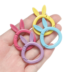Hand holding four colorful rabbit-ear metal spring ring buckles in pastel matte finish