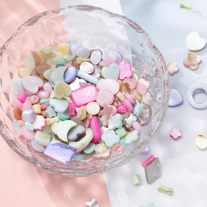 Macro shot of colorful iridescent heart and star shell beads in a glass bowl for DIY jewelry