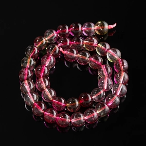 Close-up of polished watermelon tourmaline beads with natural texture on black background