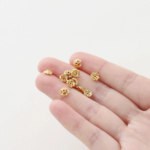 Nahaufnahme von 18K vergoldeten Hohlblumen-Zwischenperlen für DIY-Schmuck auf Fingerspitzen