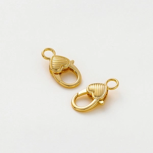 Dettaglio di due chiusure a moschettone a cuore placcate oro 14K con texture in rilievo