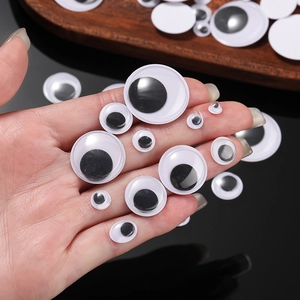 Various sizes of adhesive googly eyes for DIY crafts held in hand on a wooden tray