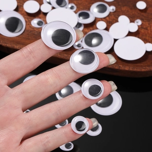 DIY googly eyes stickers in various sizes held on a fingertip for craft doll projects